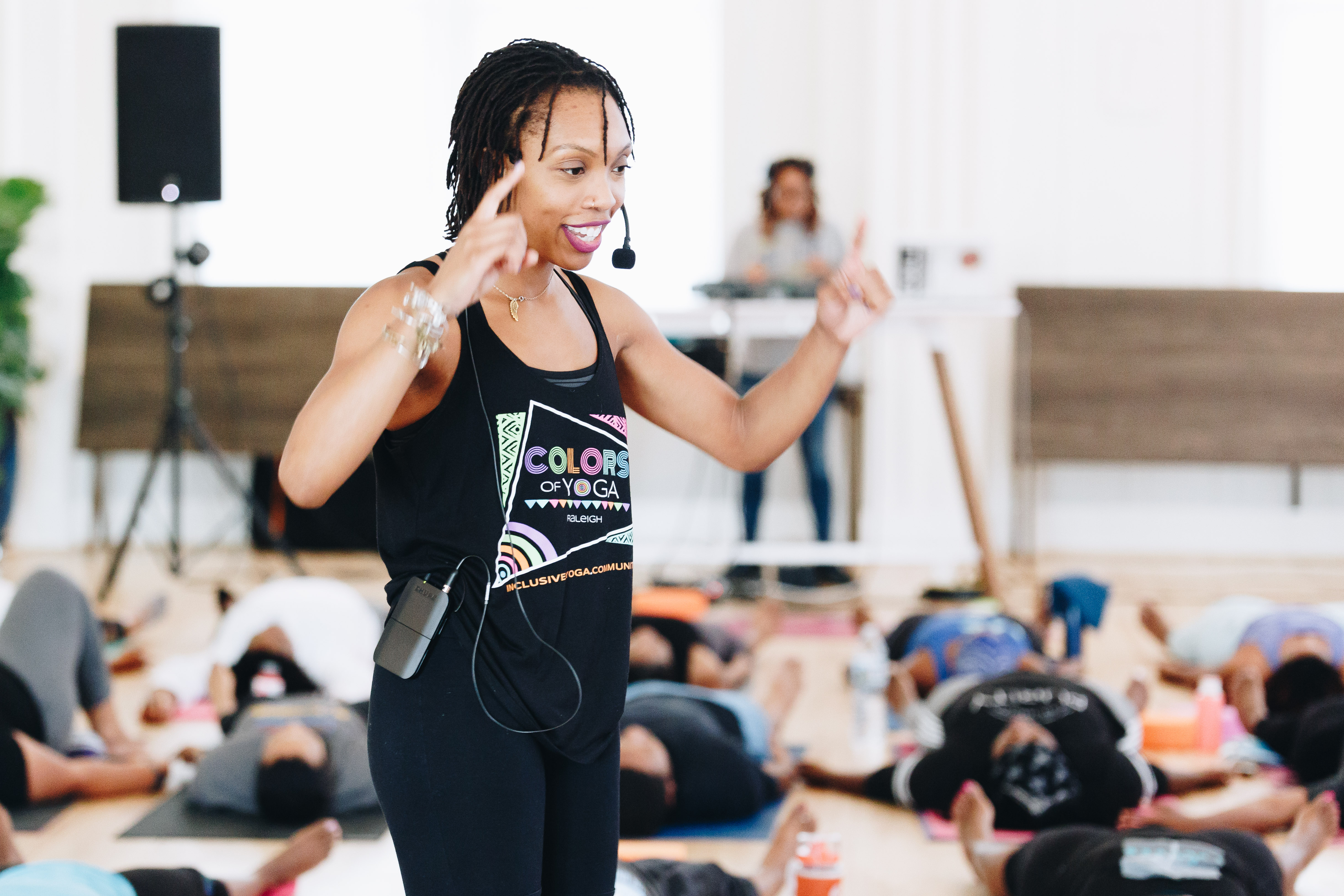 Black woman with short hair and microphone leading yoga class