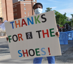 woman in hospital attire holding "thanks for the shoes" sign