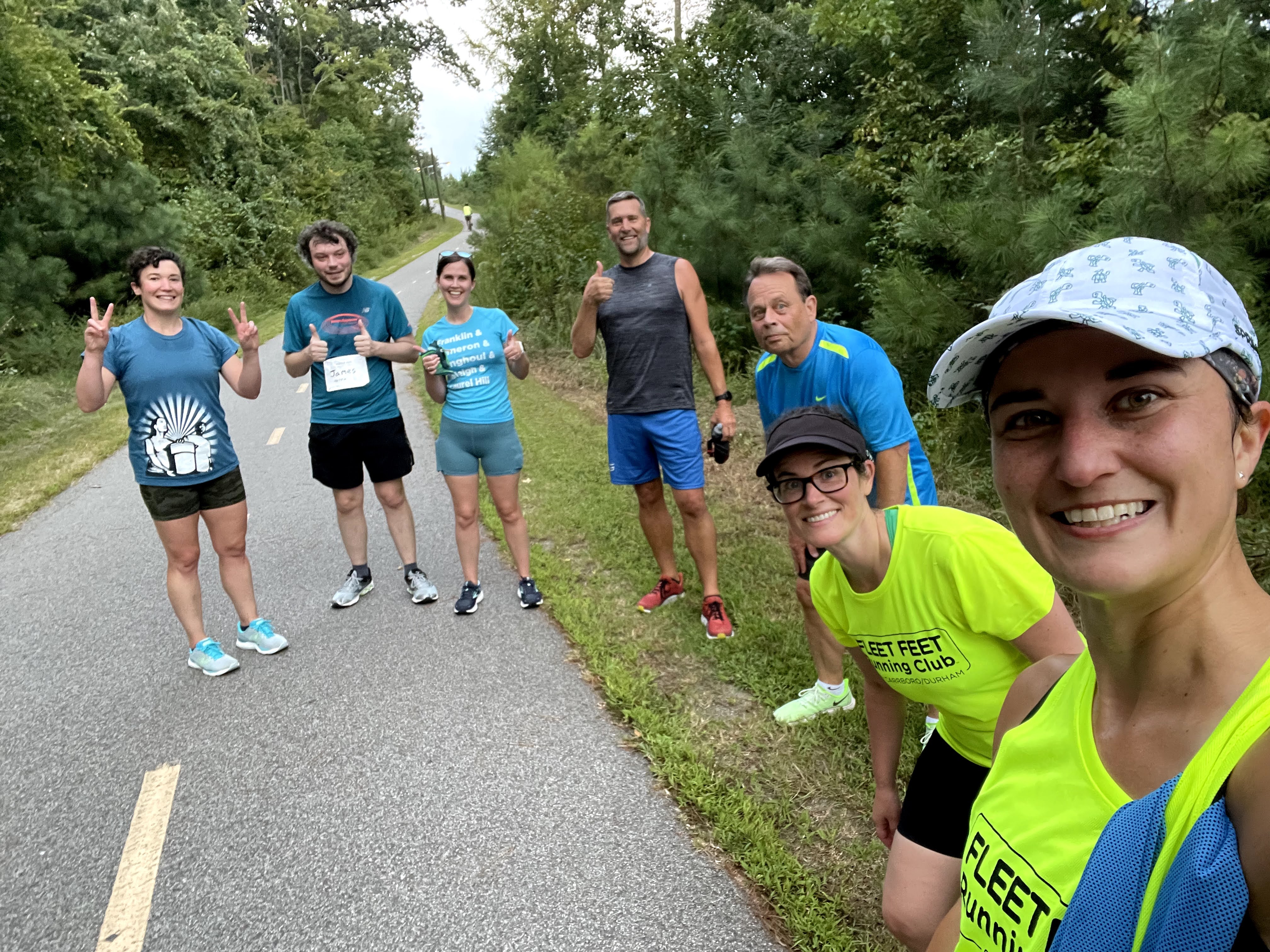 Group of smiling runners and walkers at the base of a hill