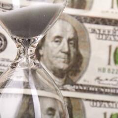 One hundred dollar bills behind an hour glass containing white sand