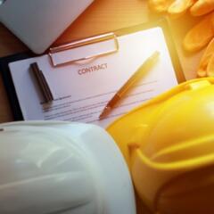 2 hard hats, a contract, gloves, and laptop on desk