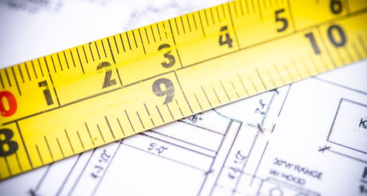 A close-up view of a yellow measuring tape placed over intricate architectural blueprints
