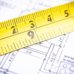 A close-up view of a yellow measuring tape placed over intricate architectural blueprints