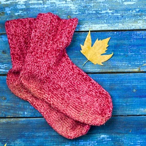 A pair of red socks with a yellow leaf on blue wooden background