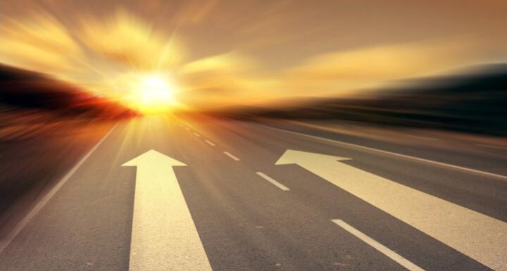 Arrows on a road pointing towards the sunrise signifying growth and new direction