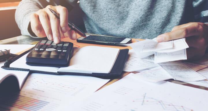 Bankruptcy bills covering a desktop along with a smartphone and a hand typing on a calculator