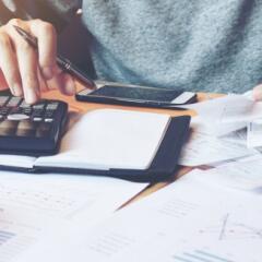 Bankruptcy bills covering a desktop along with a smartphone and a hand typing on a calculator