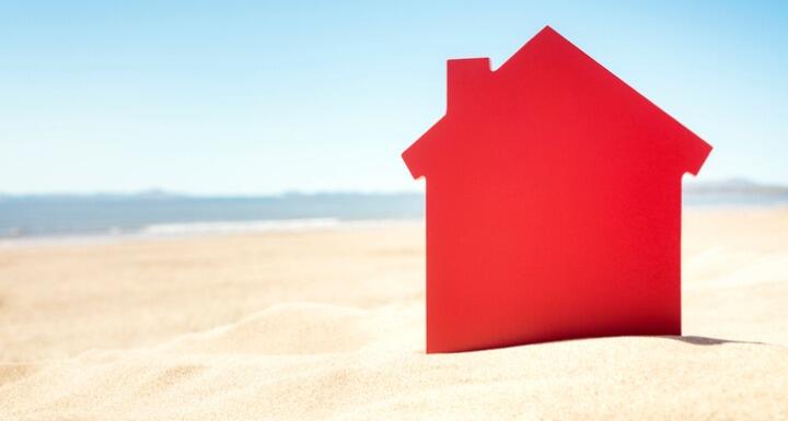 Red house cutout sticking out of sand on the beach