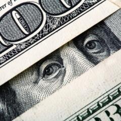 Close up of one hundred dollar bills arranged so it looks like Ben Franklin is peeking at the viewer