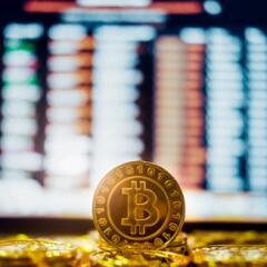 A gold coin stamped with a bitcoin logo in front of a computer screen