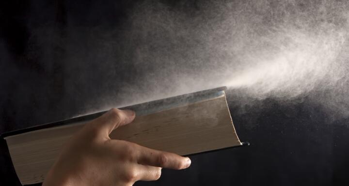 Boy blows dust off book.