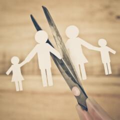 Small paper doll cutouts of a family being snipped in two pieces by kitchen scissors on a wooden background