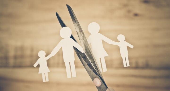 Small paper doll cutouts of a family being snipped in two pieces by kitchen scissors on a wooden background