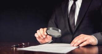 Businessman holding magnifying glass over document