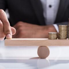 Businessperson Balancing Stacked Coins On Wooden Seesaw