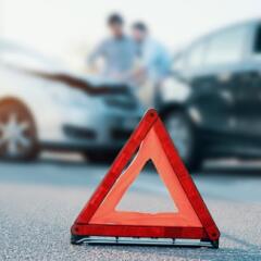 An orange caution pop up sign placed on the road with a two car accident in the background