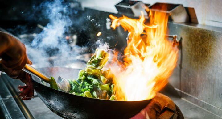 Chef in restaurant kitchen at stove with high burning flames