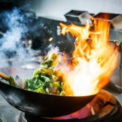 Chef in restaurant kitchen at stove with high burning flames