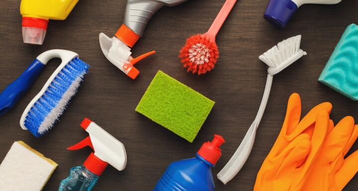 Multiple cleaning products laying on a brown table including several spray bottles and various cleaning brushes