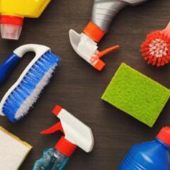Multiple cleaning products laying on a brown table including several spray bottles and various cleaning brushes