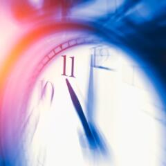 Blurred clock with the hands showing eleven o'clock