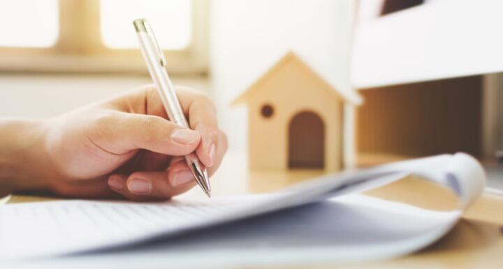Close up hand of a man signing a signature document with an image of a house in the background