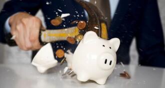 Close-up of businessman using a hammer to smash plenty of coins inside piggybank into pieces as he needs emergency money