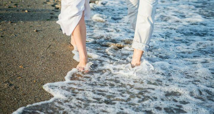 Close up of two people wearing white walking on beach