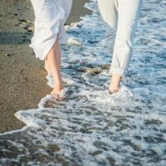 Close up of two people wearing white walking on beach