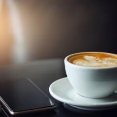 Closeup latte art coffee in white cup with smartphone and notebook on black table