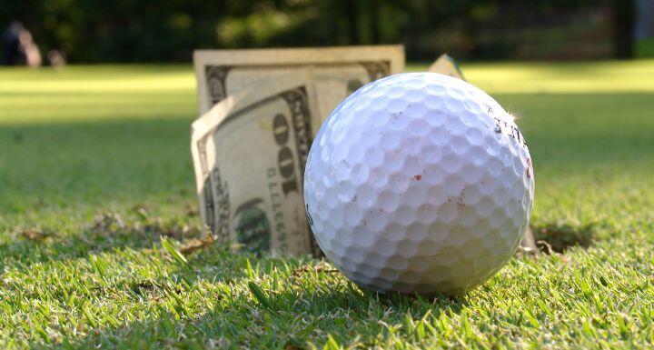 Closeup of golf ball by hole with $100 bills sticking out
