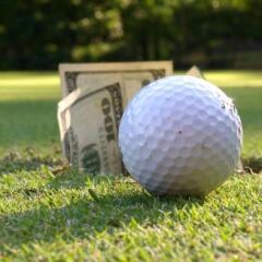 Closeup of golf ball by hole with $100 bills sticking out