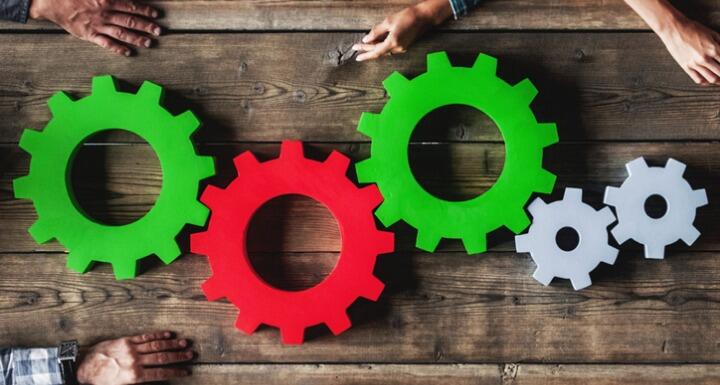 Green, red, and gray cogs and gears on wooden table