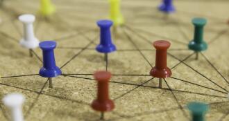 Colorful push pins connected by string on cork board