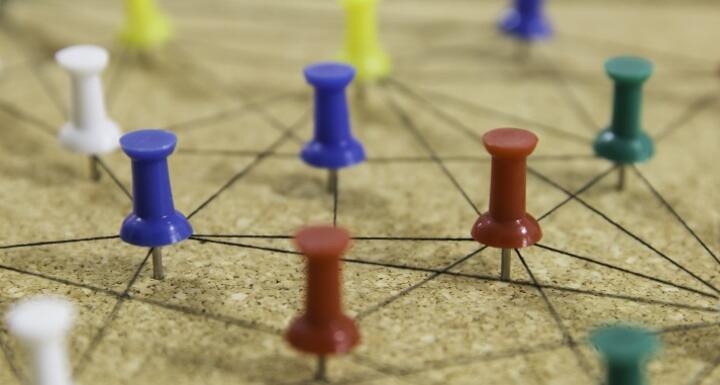 Colorful push pins connected by string on cork board