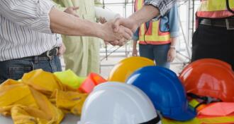 Construction group shaking hands with hardhats in foreground