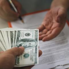 Person paying money in the form of one hundred dollar bills to another person