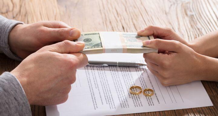 Couple's Hand Holding Currency Over The Divorce Agreement