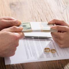 Couple's Hand Holding Currency Over The Divorce Agreement