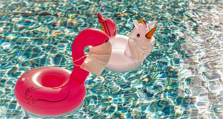 Two whimsical pool floats in a pool, with the floating characters wearing medical facemasks