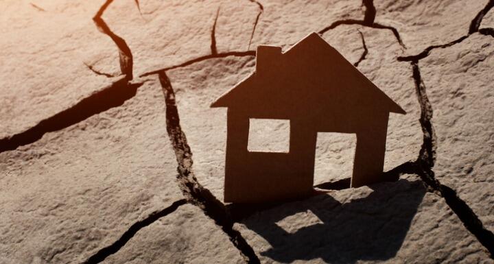 Paper house sticking out of a piece of land that is dried and cracked