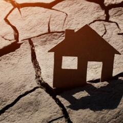 Paper house sticking out of a piece of land that is dried and cracked