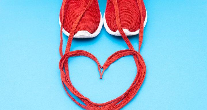 Crop view of red athletic sneakers and a heart symbol made of the shoelaces on a blue background