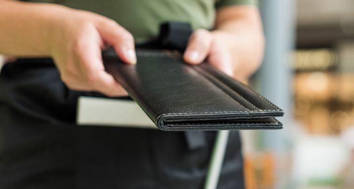 Cropped image of woman waitress in apron hold out bill folder