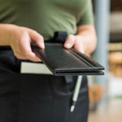 Cropped image of woman waitress in apron hold out bill folder