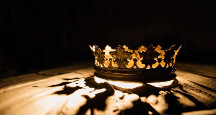 Gold crown sitting on a table with it's shadow reflecting on the table