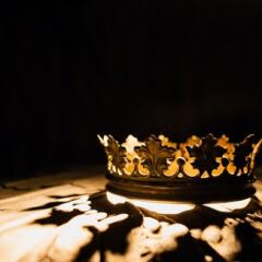Gold crown sitting on a table with it's shadow reflecting on the table
