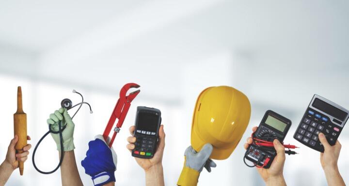 Hands holding tools of different jobs such as calculators, wrenches, and electrical equipment arranged on a white background