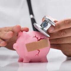 doctor examining cracked piggy bank with bandaid