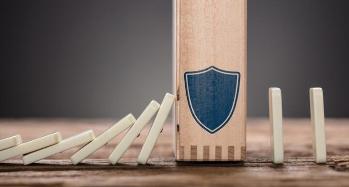 Wooden dominos falling into larger domino with blue shield